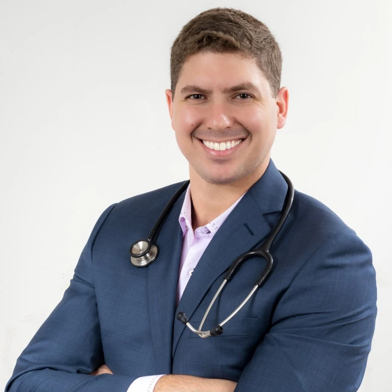 Retrato de médico sorridente de terno azul, estetoscópio ao pescoço, braços cruzados