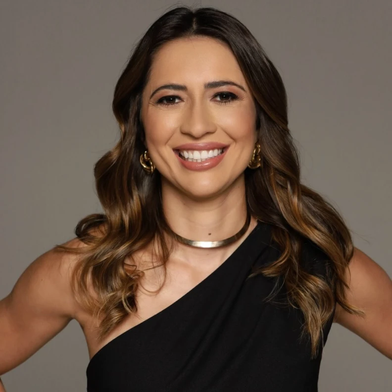 Retrato de mulher sorridente de cabelo castanho ondulado e vestido preto assimétrico