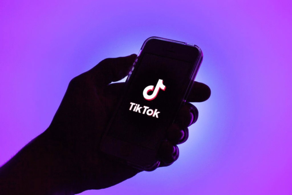 Silhueta de mão segurando celular com o logo do TikTok, em fundo roxo
