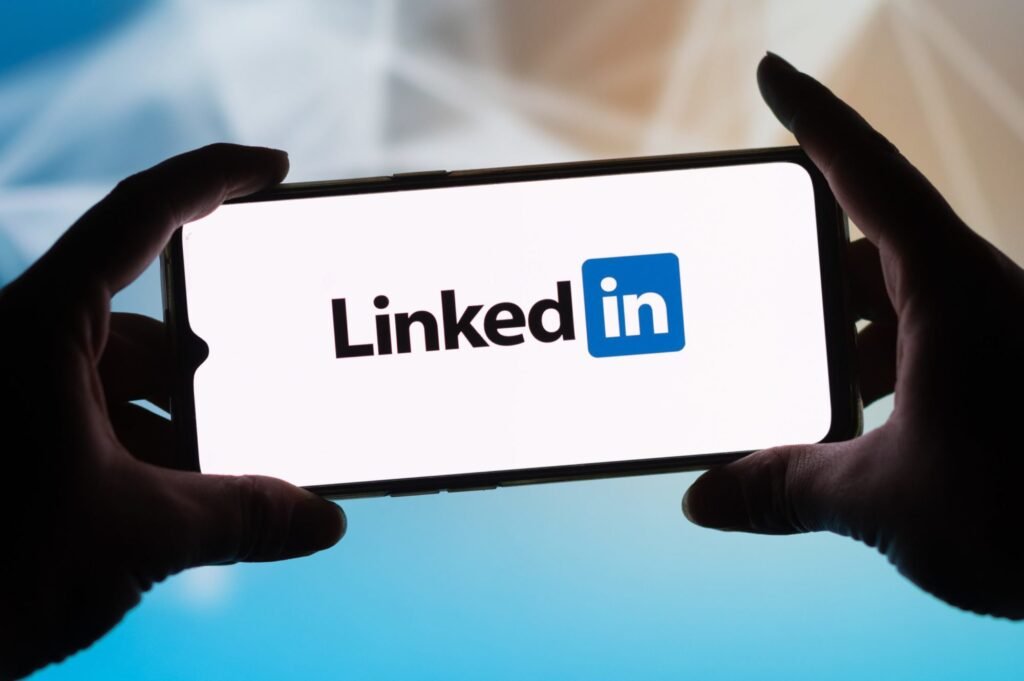 Mãos seguram celular exibindo a tela inicial do LinkedIn