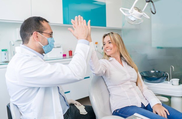 Dentista de máscara e paciente sorridente batem a mão em consultório odontológico