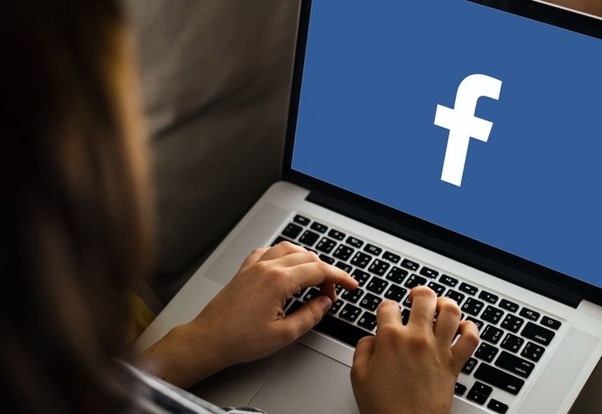 Mãos digitam em notebook com o logo do Facebook na tela