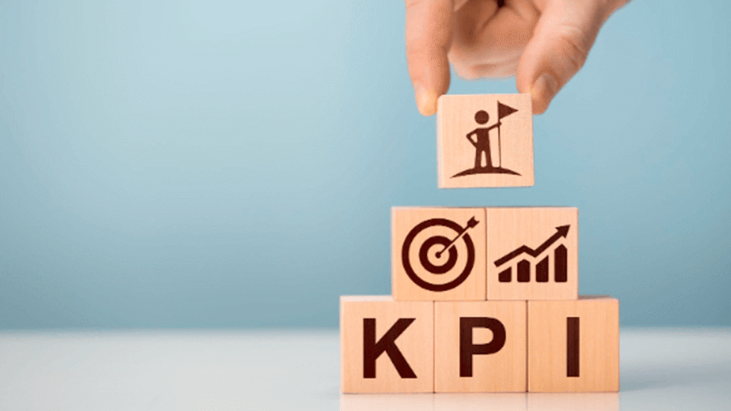 Mão empilha blocos de madeira formando a palavra KPI com ícones de meta e crescimento