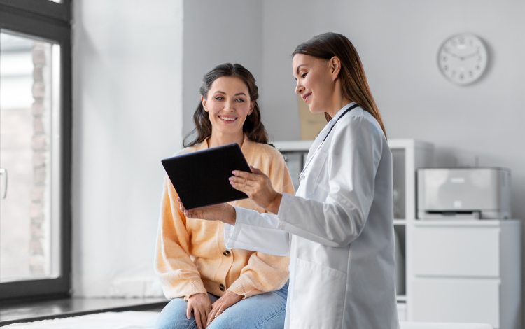 Médica mostra resultado em tablet a paciente sorridente em consultório