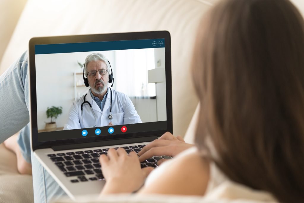 Paciente deitada faz teleconsulta por videochamada com médico em notebook