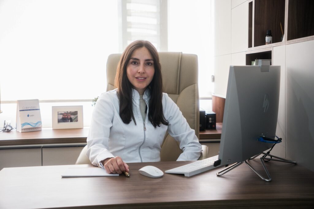 Médica sorridente sentada à mesa do consultório em frente a um monitor