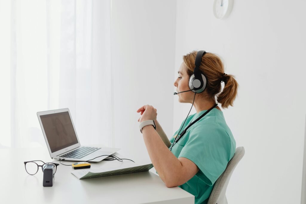 Profissional de scrubs verde-água com headset atende chamada em frente ao notebook