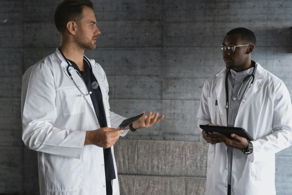 Dois médicos de jaleco branco conversam segurando tablet e radiografia em corredor