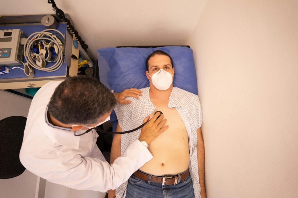 Médico ausculta o peito de um paciente de máscara deitado em maca de hospital