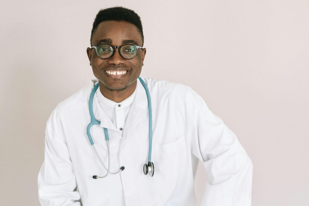 Médico sorridente de óculos e estetoscópio azul-petróleo posa em fundo neutro