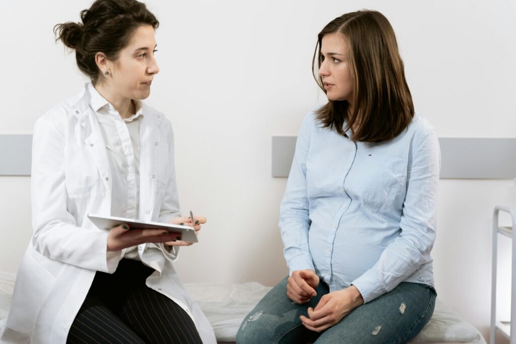 Médica conversa com paciente grávida sentada em maca de consultório