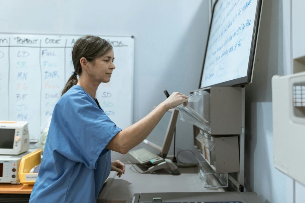 Enfermeira de scrubs azul organiza medicamentos em painel na central de enfermagem