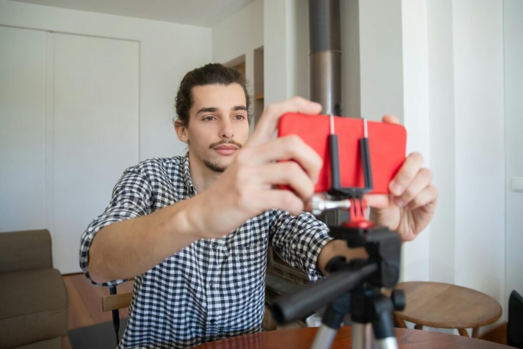 Homem ajusta celular vermelho em suporte de tripé para gravar vídeo