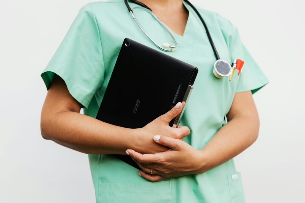 Profissional de scrubs verde-água segura tablet preto junto ao corpo, com estetoscópio ao pescoço