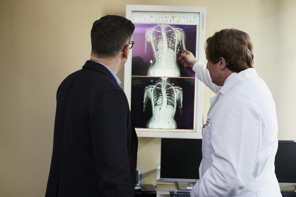 Médico aponta para radiografias de coluna em negatoscópio ao explicar a um paciente de terno