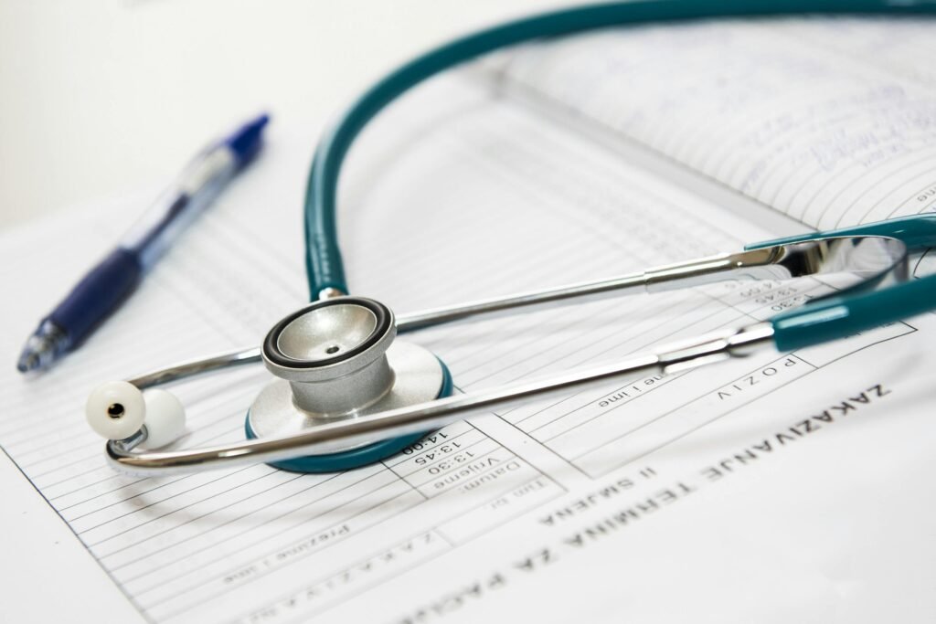 Estetoscópio azul-petróleo sobre formulários médicos, ao lado de uma caneta