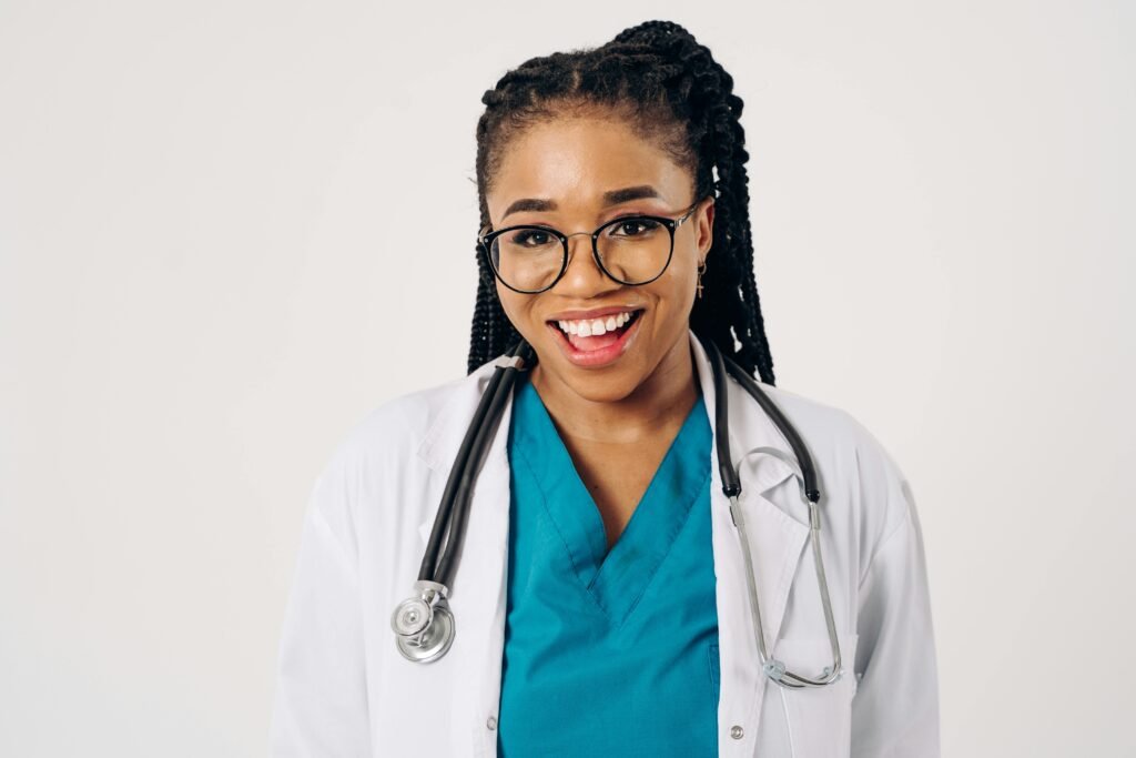 Médica sorridente de óculos, scrubs azul-petróleo e estetoscópio ao pescoço