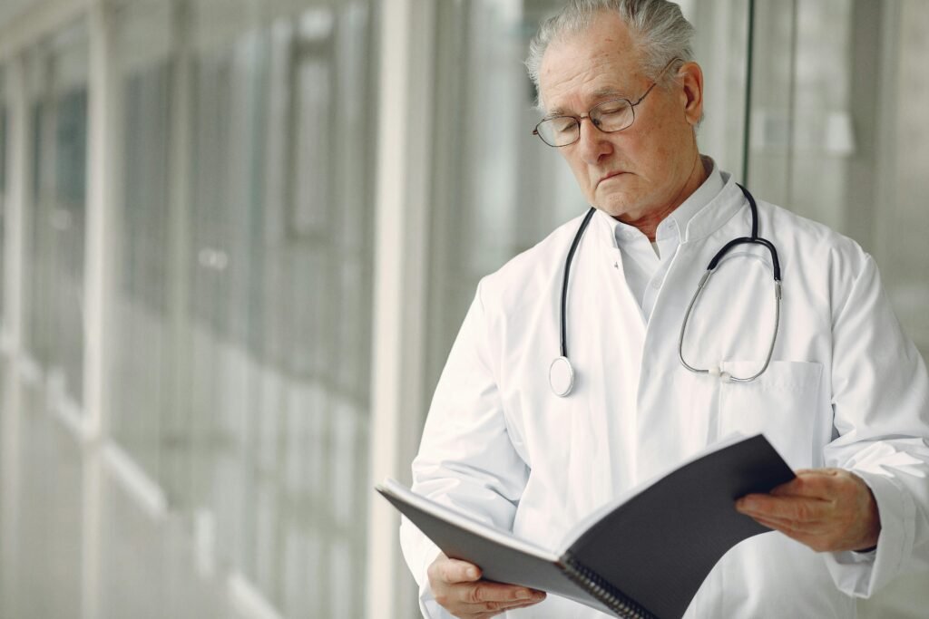 Médico idoso de jaleco branco lê anotações em caderno enquanto caminha por corredor