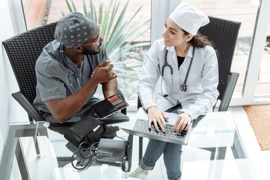 Médico e médica conversam animadamente sobre laptop e itens de aferição de pressão em mesa de vidro