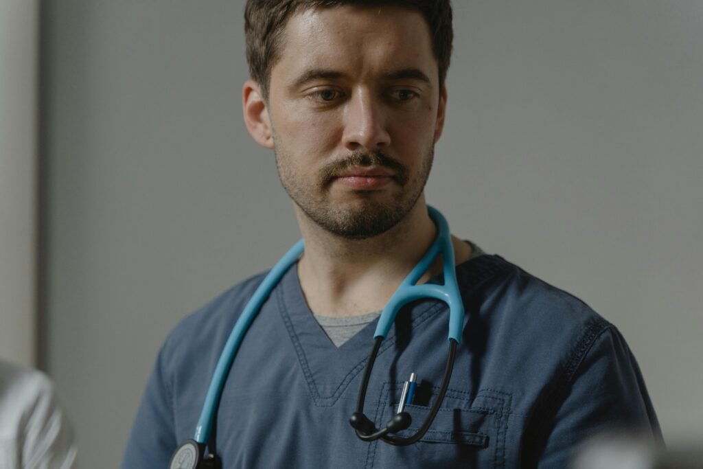 Médico de scrubs azul-marinho com estetoscópio ao pescoço, expressão séria