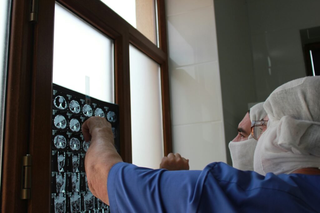 Médico aponta para exames de tomografia em negatoscópio junto de colega de scrubs azul