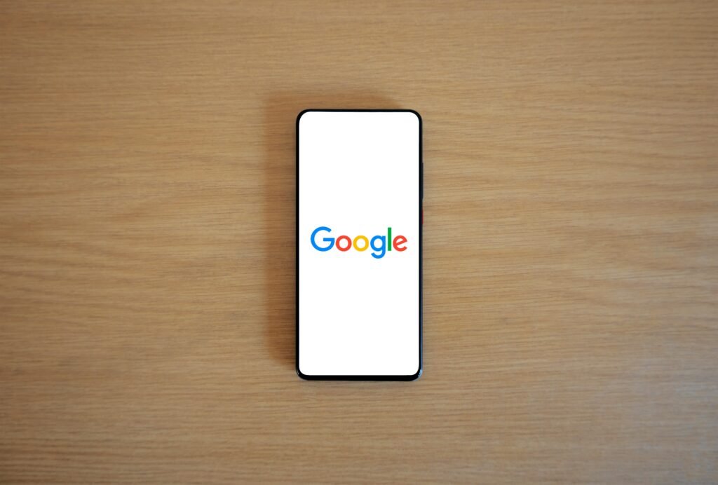Celular sobre mesa de madeira exibindo a logo do Google na tela
