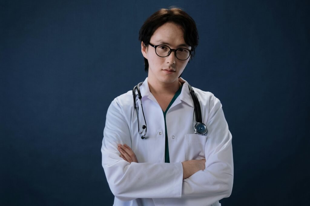 Médico de óculos e estetoscópio posa de braços cruzados em fundo azul