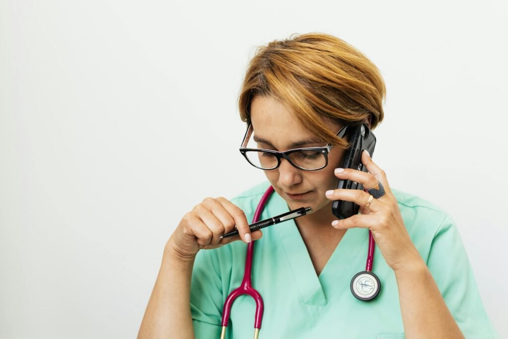 Enfermeira de scrubs verdes fala ao telefone enquanto segura uma caneta