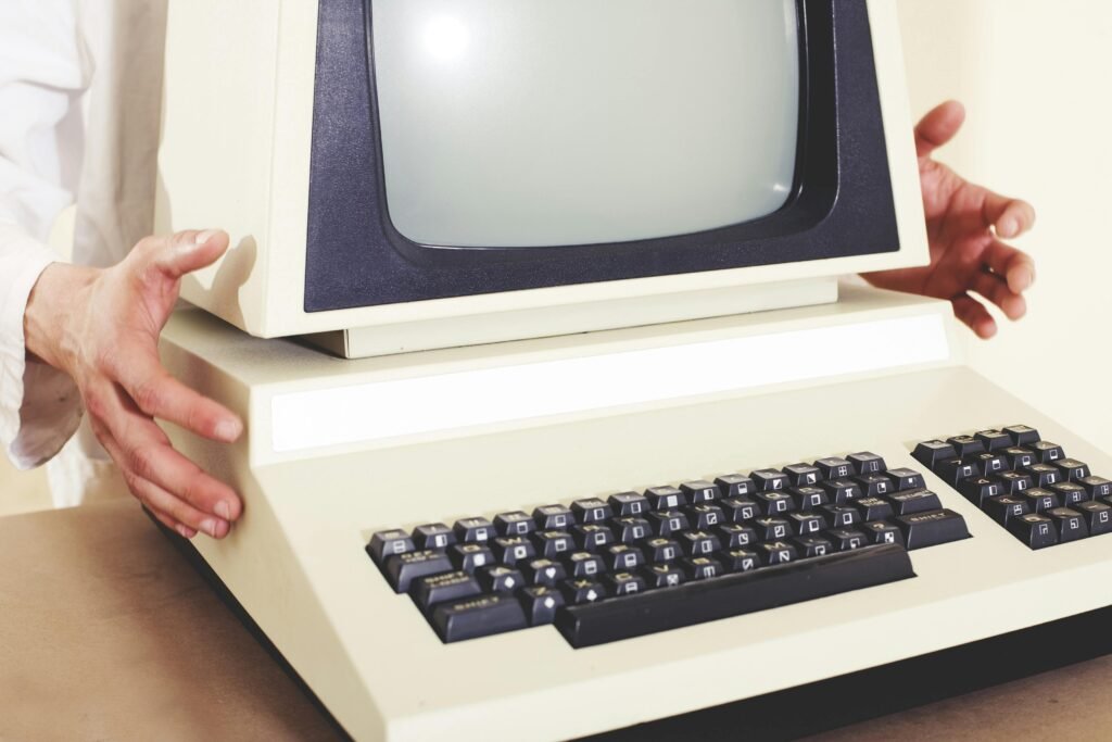 Mãos apontam para um computador antigo de mesa com monitor CRT e teclado retrô