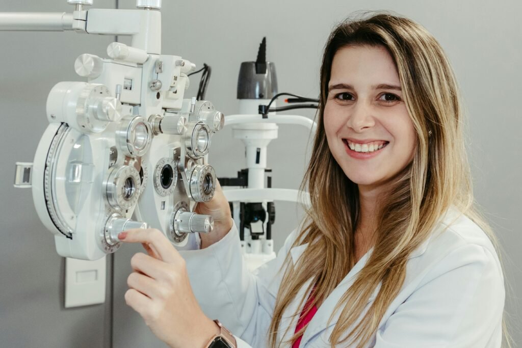 Oftalmologista sorridente ao lado de aparelho de refração ocular (foróptero) em consultório