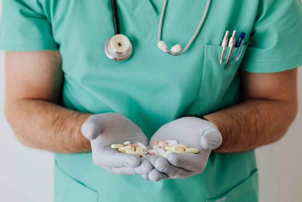 Profissional de saúde de scrubs verdes segura comprimidos coloridos nas mãos com luvas