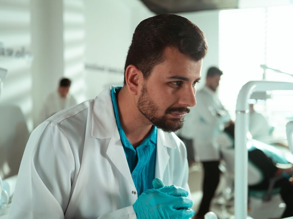 Dentista de luvas e jaleco branco atento durante procedimento em clínica odontológica