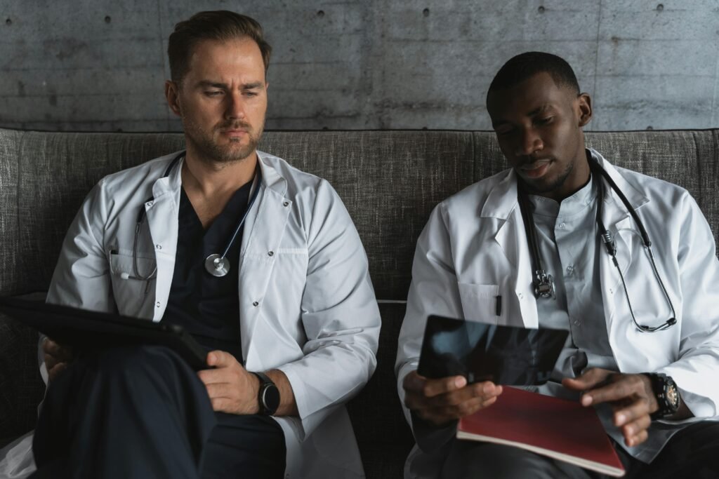 Dois médicos de jaleco branco sentados em sofá, um deles analisando radiografia em tablet