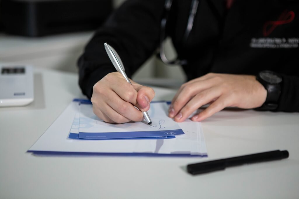 Mão de profissional de saúde assinando documento em prancheta sobre a mesa do consultório
